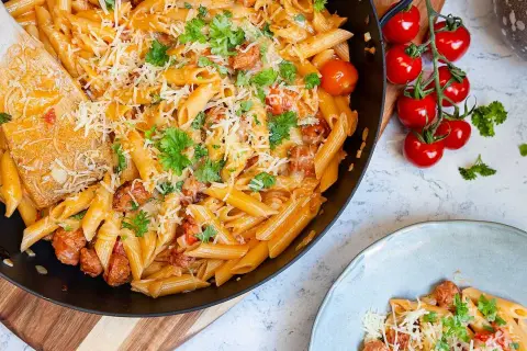 En stor panna med krämig pasta med chorizo, toppad med riven ost och färsk persilja. Bredvid syns en tallrik med samma läckra pasta.
