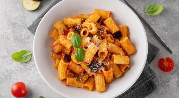 En skål med pasta norma, en klassisk siciliansk rätt med aubergine och tomatsås, toppad med basilika och parmesan.