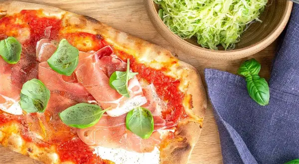 Pizza med prosciutto och basilika, perfekt till ett burrata recept. Bredvid en skål med krispig sallad.