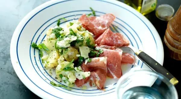 En tallrik med potatissallad med parmesan, serverad med salami och prosciutto. En utsökt måltid!
