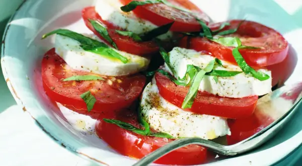 En Caprese-sallad med skivade tomater och mozzarella liknande ost, garnerad med färsk basilika och peppar.