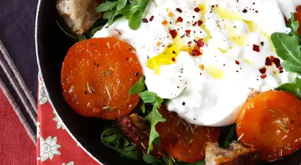 En krämig italiensk ost burrata serveras med ugnsrostade tomater, ruccola och krutonger.
