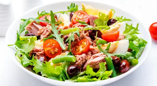 En fräsch sallad nicoise med tonfisk, ägg, tomater, oliver och gröna bönor på en bädd av sallad.