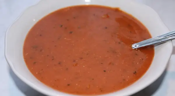 En skål med värmande linssoppa, perfekt för ett enkelt linssoppa recept. En sked vilar i den mustiga, röda soppan.