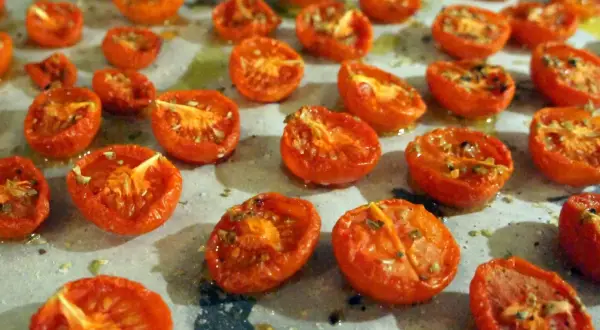 Halverade, semitorkade tomater ligger utspridda på en bakplåt. De ser saftiga och smakrika ut, redo att användas i matlagning.