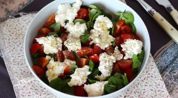 En fräsch sallad med tomater, gröna blad och krämig burrata buffelmozzarella, toppad med olivolja och svartpeppar.