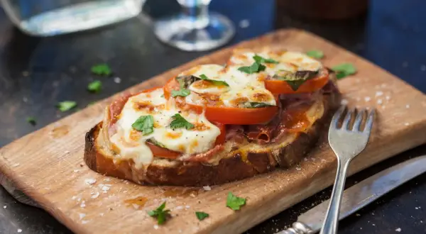 En härlig italiensk macka med smält ost, tomat och prosciutto på en träskärbräda.
