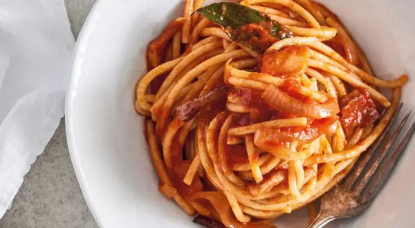 En skål med bucatini all'amatriciana, en klassisk italiensk pastarätt med tomatsås, lök och en lagerblad.