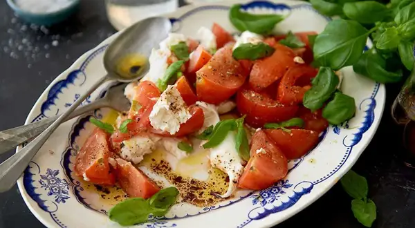 En härlig caprese sallad med saftiga tomater, krämig mozzarella och färsk basilika, ringlad med olivolja och balsamvinäger.