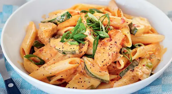 Enkel pasta med kyckling och zucchini i krämig tomatsås, toppad med salladslök.