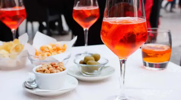 En aperitivo betyder njutning före maten. Här syns Aperol Spritz med snacks som nötter, oliver och chips.