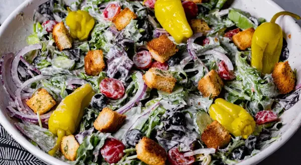 En krämig italiensk sallad till lasagne med gröna blad, tomater, rödlök, oliver, krutonger och gula peppar.
