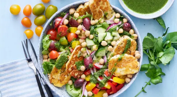 En härlig halloumi sallad med kikärtor, tomater, gurka, paprika och oliver, toppad med en grön dressing.