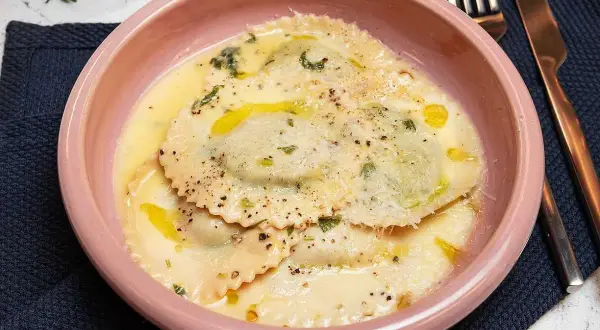 En skål med krämig ravioli, perfekt för ett enkelt ravioli recept. Garnerad med örter och parmesan.