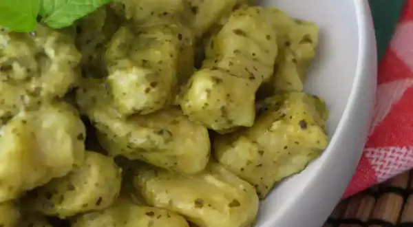En skål med krämiga gnocchi pasta med pesto och en myntakvist.
