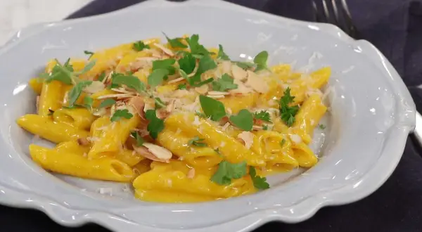 En krämig pasta milanese med mandelspån och färska örter, serverad i en ljusblå skål.