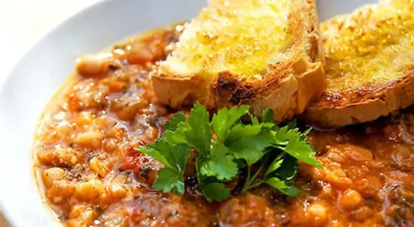 En mustig gryta med bönor och tomater, toppad med rostat bröd och persilja. Perfekt för ett enkelt svartkål recept.