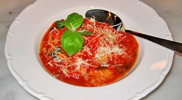 En portion pappa al pomodoro, en mustig tomatsoppa med bröd, toppad med basilika och parmesan. En sked ligger i skålen.
