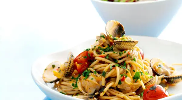 En tallrik med spaghetti vongole, toppad med färska musslor, körsbärstomater och persilja. En härlig italiensk rätt.