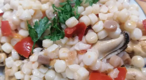 En närbild på en tallrik med fregola pasta, musslor och tärnad tomat, toppad med färsk persilja.