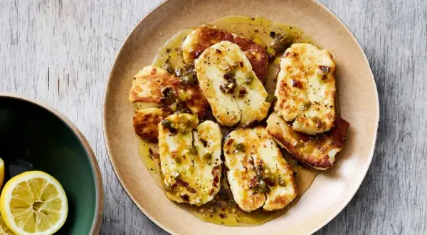 Stekt, marinerad halloumi med en kryddig dressing och chiliflakes. Serveras på en tallrik med citronklyftor vid sidan.