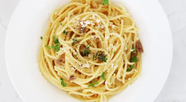En tallrik med spaghetti, toppad med riven ost, färsk persilja och små bitar av sardeller. Enkel och smakrik pasta med sardeller.