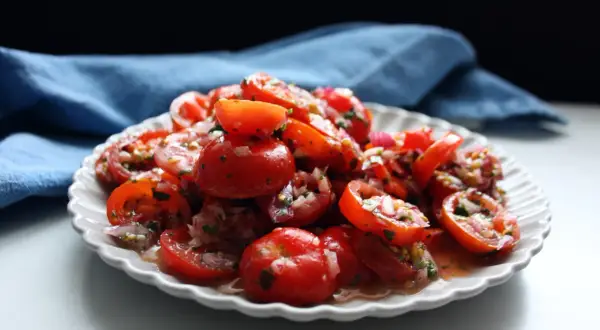 En härlig tomat sallad med rödlök och örter, serverad på en vit, mönstrad tallrik.