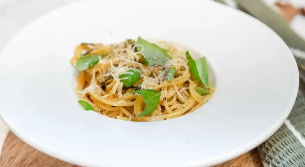 En krämig portion spaghetti alla nerano, toppad med färsk basilika och riven parmesan.