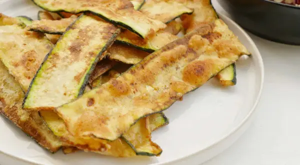 Krispiga, gyllene skivor av friterad zucchini ligger staplade på en vit tallrik, redo att avnjutas som ett lätt tilltugg.