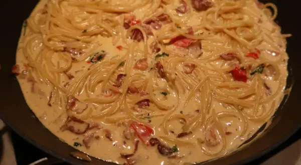 Krämig baconpasta i en stekpanna, med spaghetti och bitar av knaperstekt bacon.