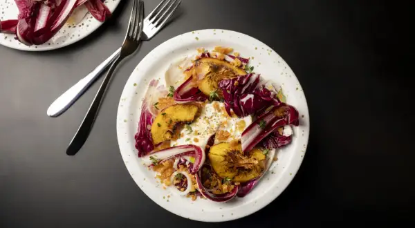 En tallrik med grillad persika, krämig burrata, krispig radicchio och örter. En utsökt sommarrätt.