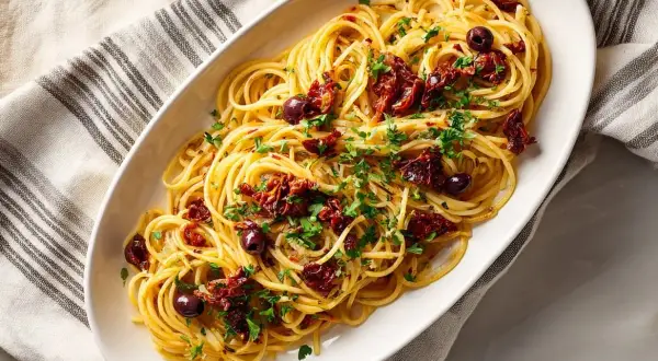 En skål med spaghetti puttanesca, toppad med soltorkade tomater, oliver och persilja.