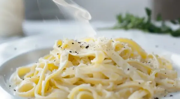 En ångande portion pasta alfredo, generöst toppad med riven parmesan och svartpeppar. Enkel men lyxig.