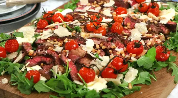 En läcker italiensk grillad biff sallad med körsbärstomater, pinjenötter och parmesan på en bädd av ruccola.
