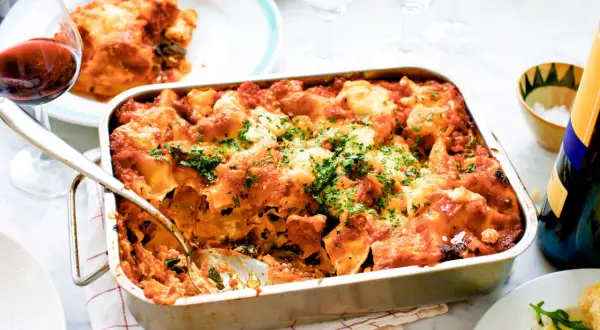 En nybakad vegetarisk lasagne i formen, toppad med ost och persilja. Ett glas rödvin står bredvid.