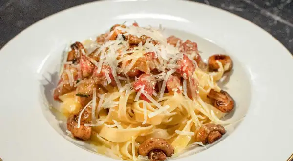 En tallrik med pasta alla boscaiola, toppad med riven parmesan och champinjoner.