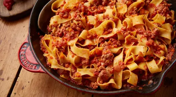 En stor portion krämig pasta bolognese i en röd gjutjärnspanna.