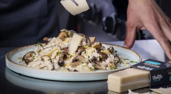 Krämig risotto svamp toppas med hyvlad ost. En vegansk ostbit ligger bredvid.