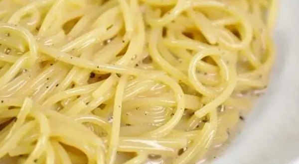 En närbild på en krämig portion spaghetti cacio e pepe, med synliga pepparkorn i den lena såsen.