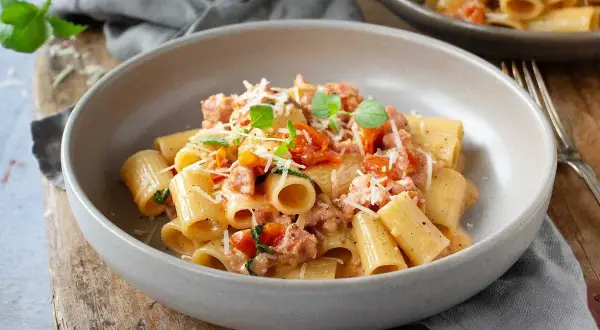 En skål med rigatoni pasta med salsicciapasta recept, toppad med riven parmesan och färsk basilika.