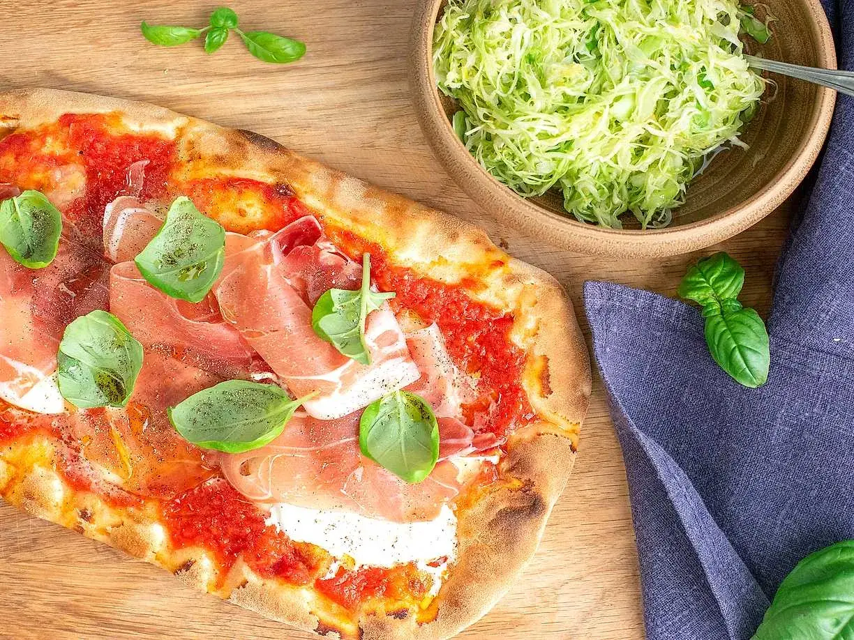 Pizza med prosciutto och basilika, perfekt till ett burrata recept. Bredvid en skål med krispig sallad.
