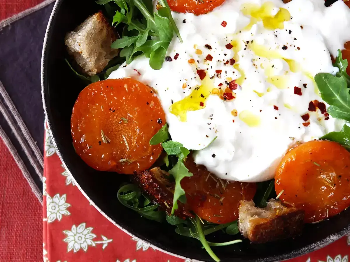 En krämig italiensk ost burrata serveras med ugnsrostade tomater, ruccola och krutonger.