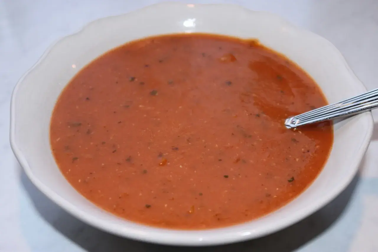En skål med värmande linssoppa, perfekt för ett enkelt linssoppa recept. En sked vilar i den mustiga, röda soppan.