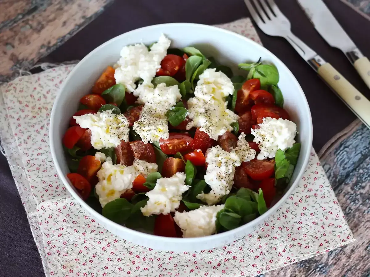 En fräsch sallad med tomater, gröna blad och krämig burrata buffelmozzarella, toppad med olivolja och svartpeppar.