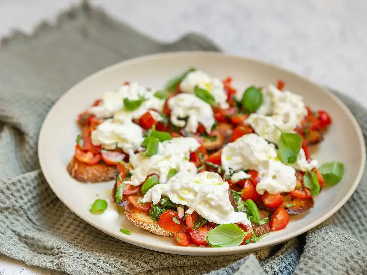 Bruschetta med burrata, färska tomater och basilika på en tallrik.