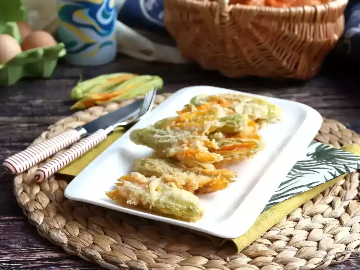 Friterad zucchini blomma serveras på en vit tallrik. Bredvid ligger en kniv och gaffel.