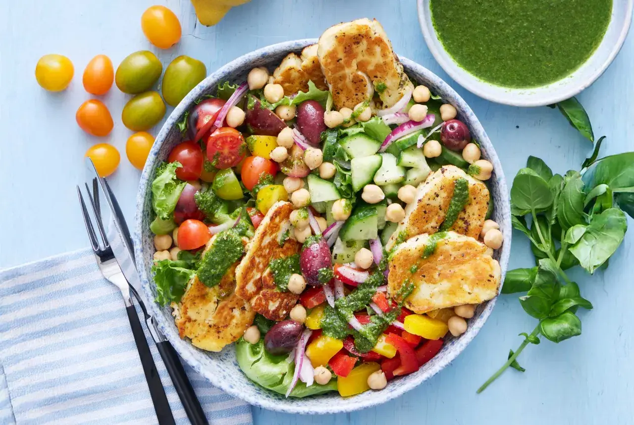 En härlig halloumi sallad med kikärtor, tomater, gurka, paprika och oliver, toppad med en grön dressing.
