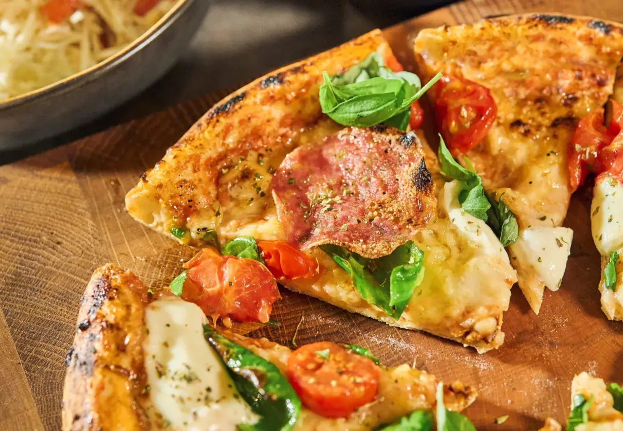 En härlig pizza Parma med salami, tomater och färsk basilika på en träskärbräda.
