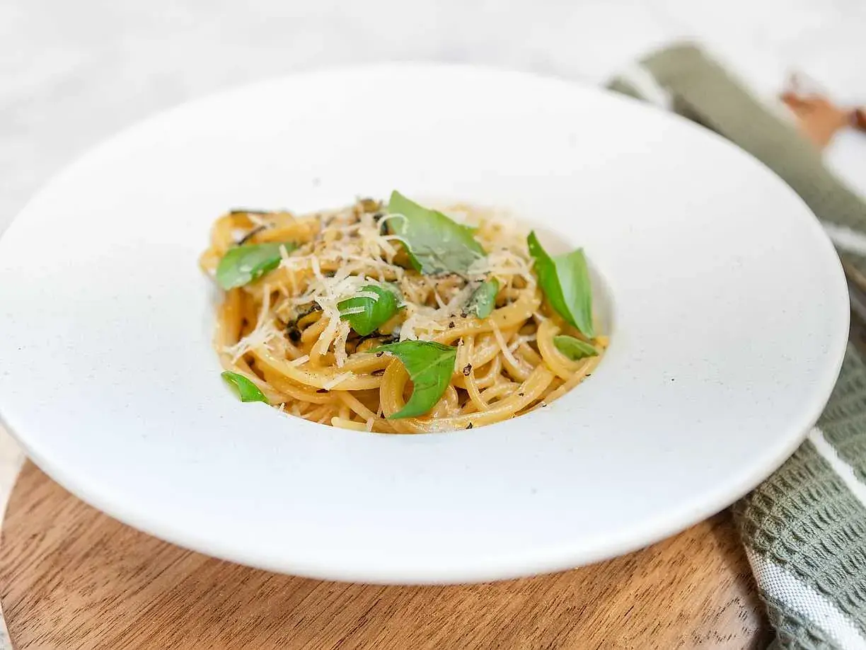 En krämig portion spaghetti alla nerano, toppad med färsk basilika och riven parmesan.