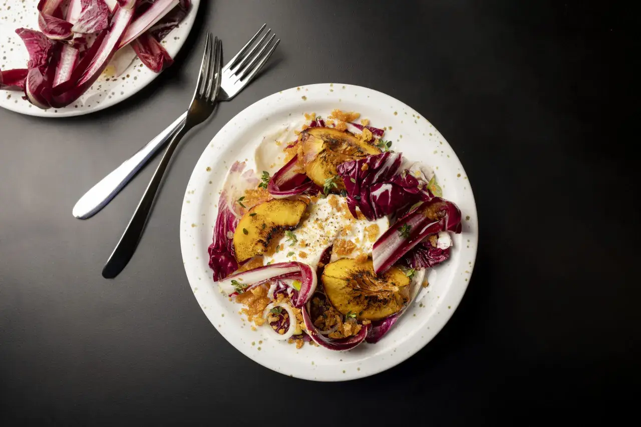 En tallrik med grillad persika, krämig burrata, krispig radicchio och örter. En utsökt sommarrätt.